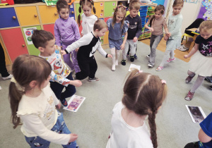 Dzieci skaczą po dywanie, na którym rozłożone są papierowe nominały pieniędzy.