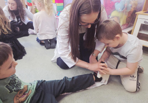 Chłopiec pod nadzorem studentki bandażuje nogę kolegi.