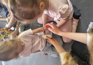 Dziewczynki z pomocą studentki bandażują sobie ręce.