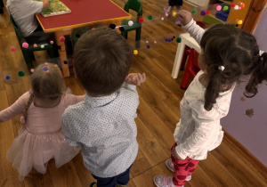 Dzieci przyklejają kolorowe pompony do rozwieszonej taśmy klejącej.
